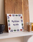 Boerenbont ceramic tile featuring "My kitchen, my rules" framed by traditional Dutch floral patterns, displayed alongside spices and kitchen accessories.