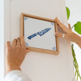Houten lijst met daarin een tegel met een koksmes, die aan een muur wordt gehangen.