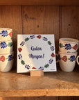 Boerenbont ceramic tile featuring the German greeting "Guten Morgen!" surrounded by traditional floral patterns, displayed with matching coffee mugs. [market:de,at]