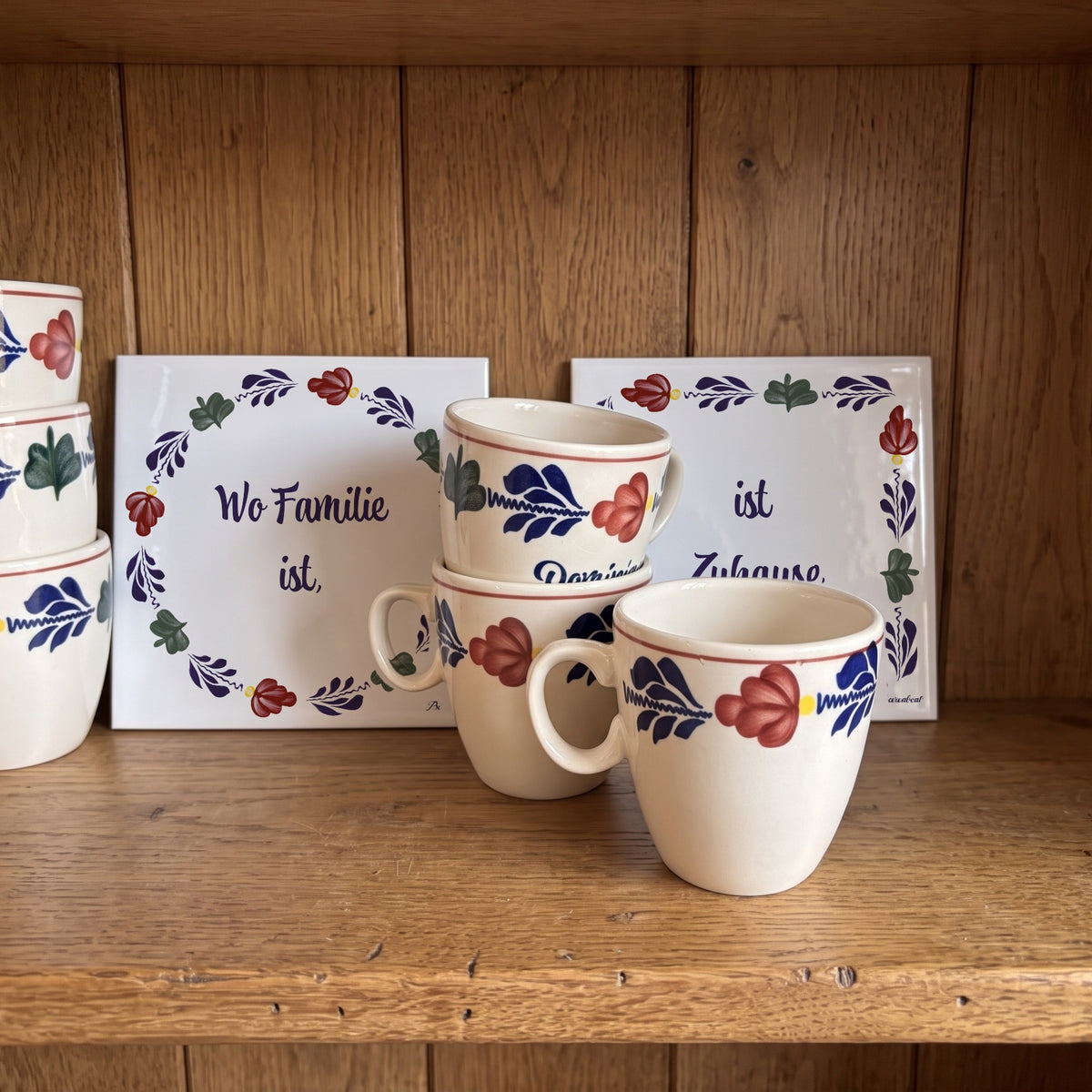 Two Boerenbont ceramic tiles featuring the German saying "Wo Familie ist, ist Zuhause", decorated with traditional Dutch floral patterns and matching coffee cups. [market:de,at]