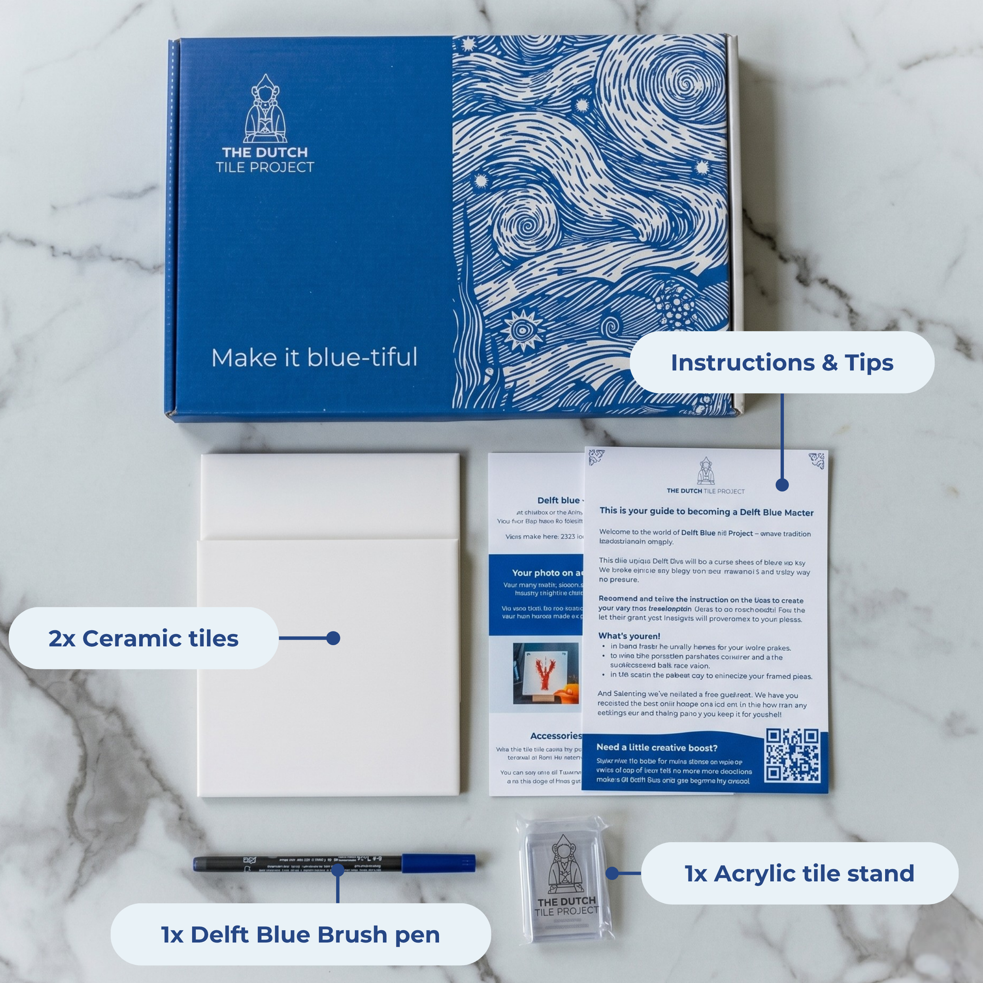 DIY kit contents displayed on a marble surface, including two ceramic tiles, a bent brush, an acrylic stand and instruction cards. [market:!nl]