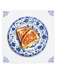 Two pieces of grilled cheese toastie on a decorative blue and white plate with floral patterns, on a dutch delft blue tile.