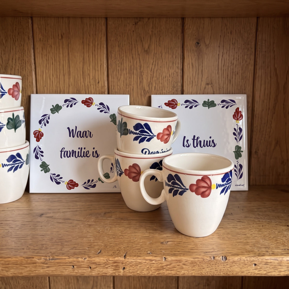 Two Boerenbont ceramic tiles featuring the Dutch saying "Waar familie is, is thuis", decorated with traditional floral patterns and displayed alongside matching coffee mugs. [market:nl]