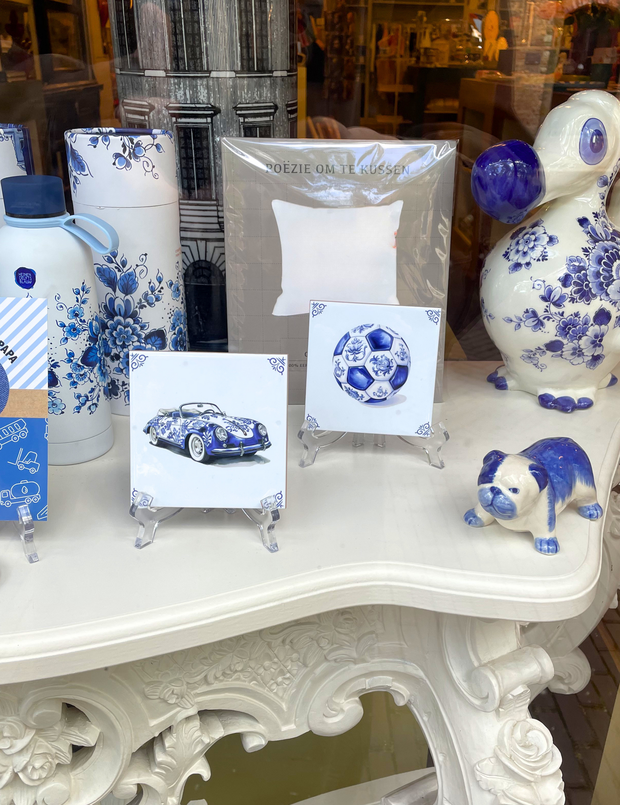 A collection of blue and white ceramic and glass mementos, including a car-themed coaster, a soccer ball coaster, a small blue dog figurine, a blue owl jar, and a blue car magnet, displayed on an ornate white table.