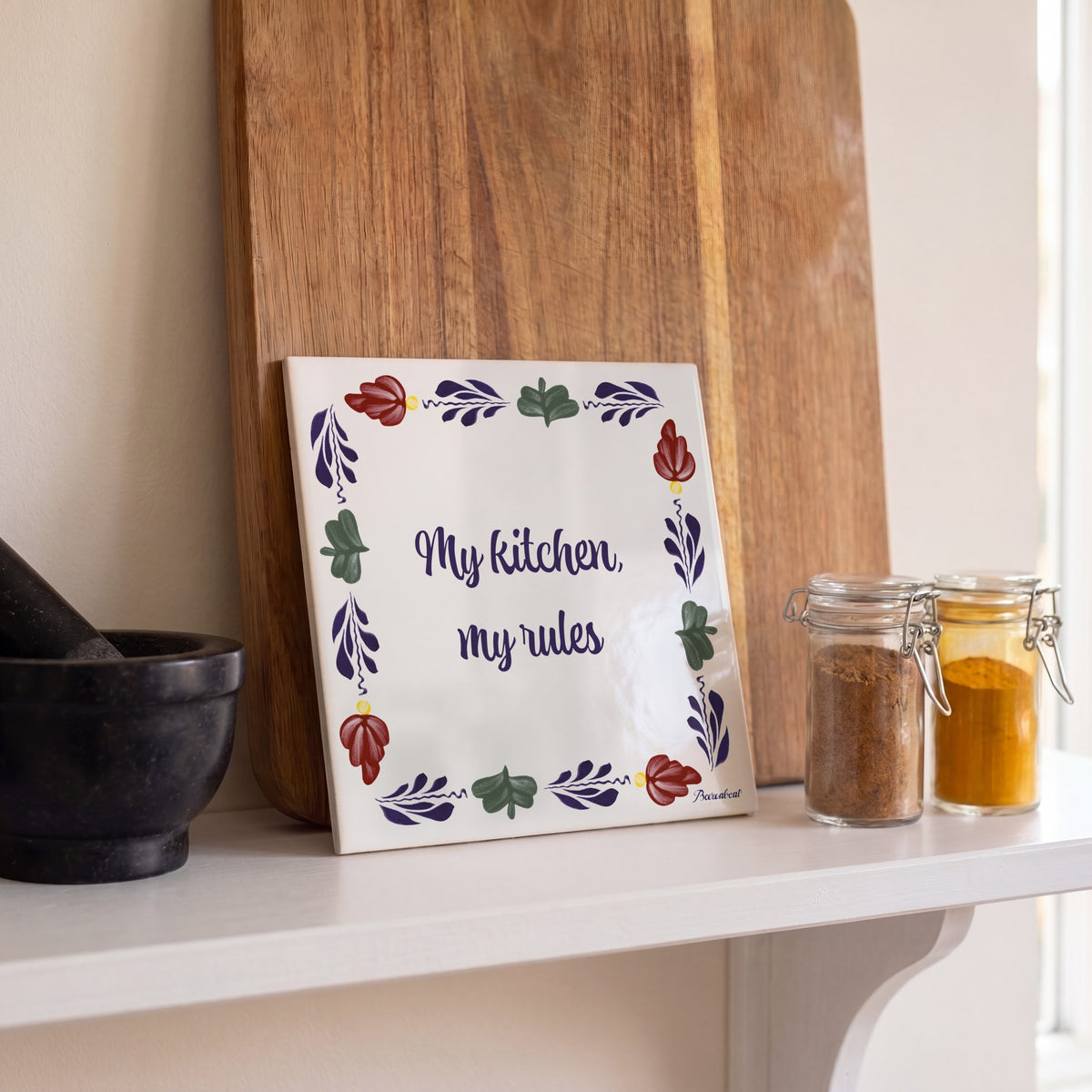 Boerenbont ceramic tile featuring "My kitchen, my rules" framed by traditional Dutch floral patterns, displayed alongside spices and kitchen accessories.