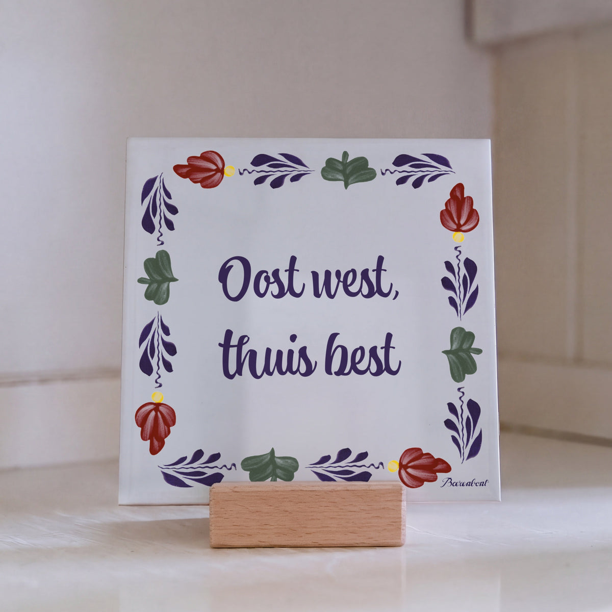 Traditional Boerenbont ceramic tile featuring the Dutch saying "Oost west, thuis best" surrounded by colourful floral motifs on a wooden tile stand.
