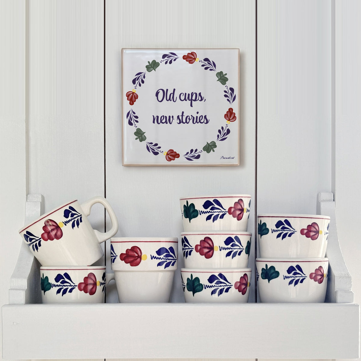 Boerenbont ceramic tile featuring "Old cups, new stories" and traditional Dutch floral motifs, displayed above a collection of matching Boerenbont cups.