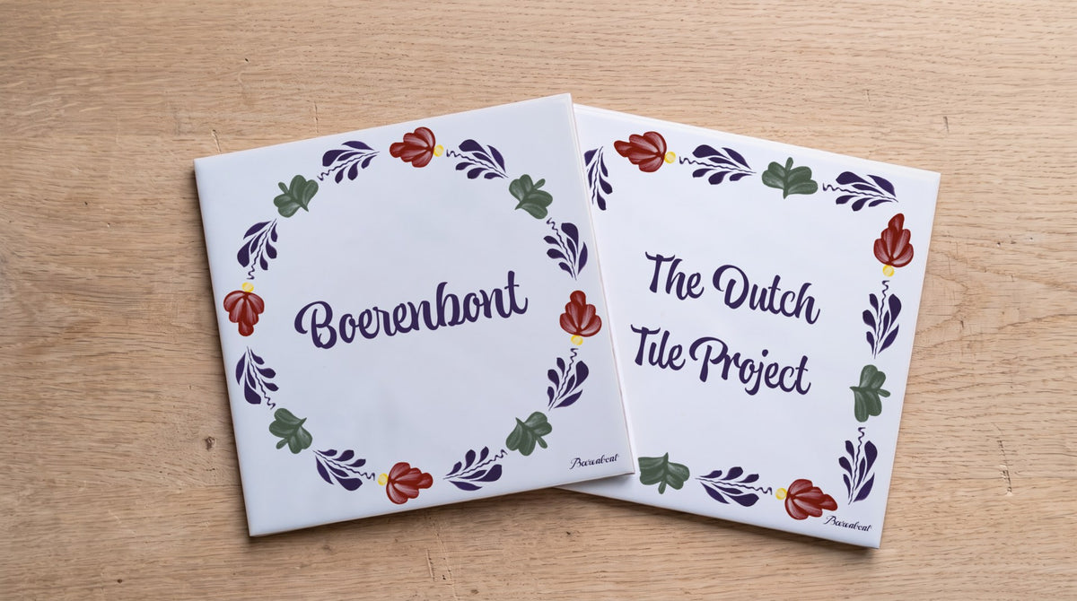 Two ceramic tiles featuring the Boerenbont and The Dutch Tile Project logos, surrounded by traditional Dutch floral patterns on a wooden table.