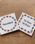Two decorative ceramic tiles featuring the Boerenbont and The Dutch Tile Project logos, surrounded by traditional Dutch floral patterns, displayed on a wooden table.
