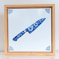 Wooden frame with a 15x15 cm chef’s knife tile inside, standing upright on a table.