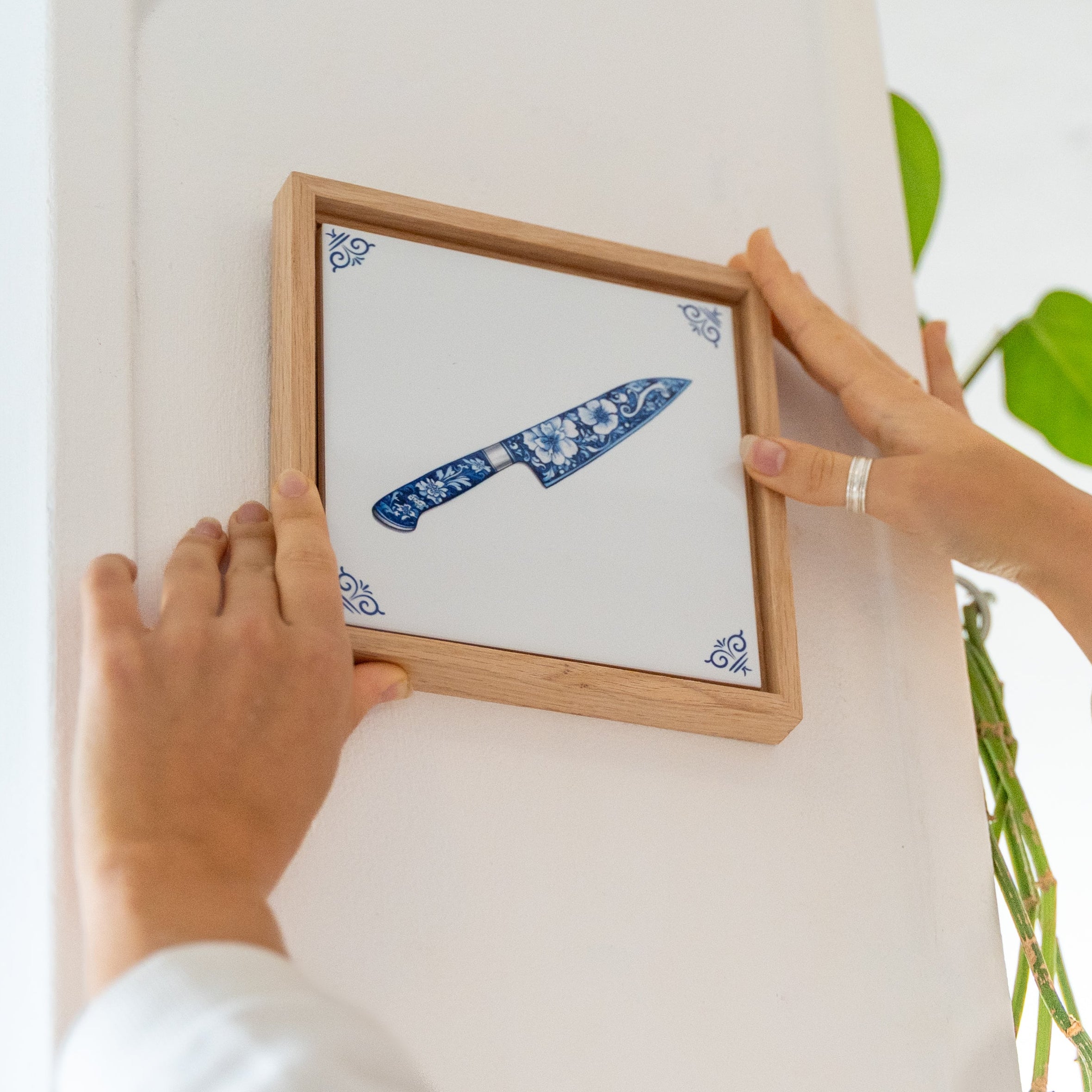 Wooden frame with a chef’s knife tile inside being hung on a wall.