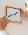 Wooden frame with a chef’s knife tile inside being hung on a wall.
