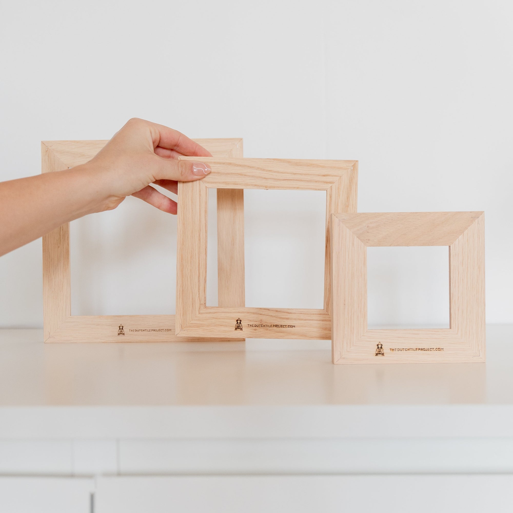 Back view of three wooden tile frames without tiles, with a hand placing the medium-sized frame upright.