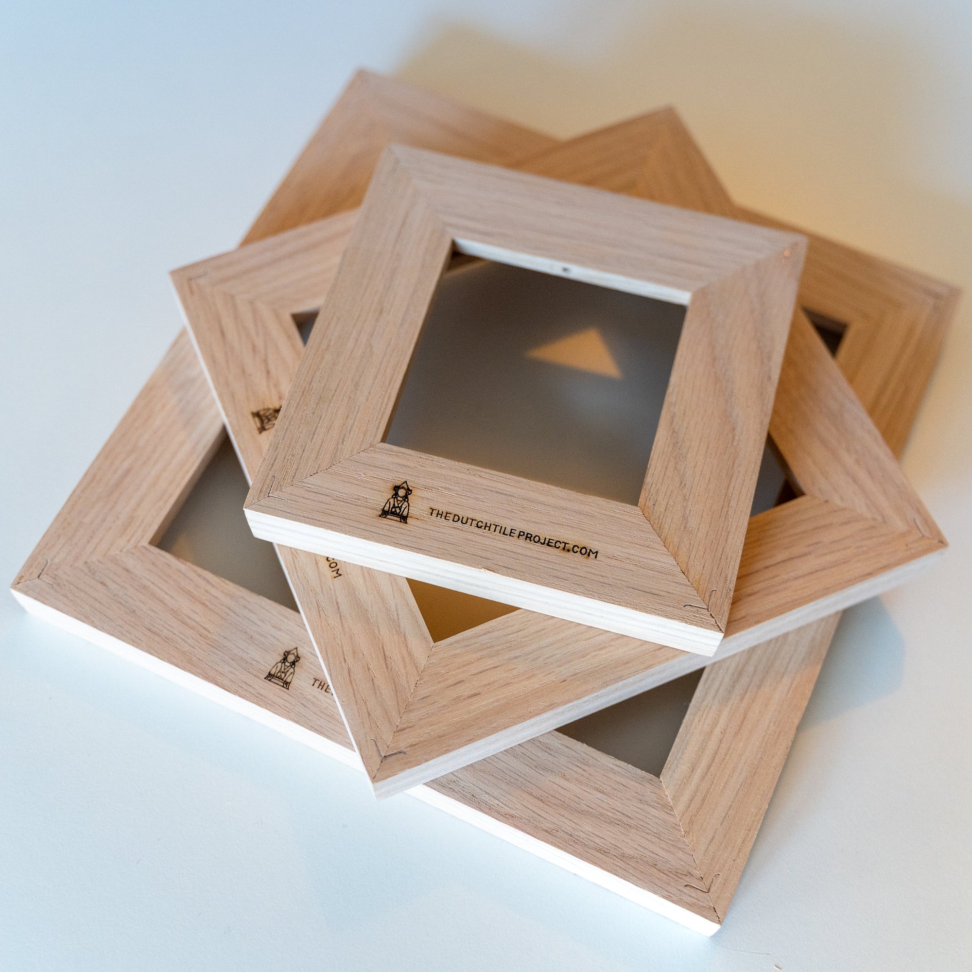 Back view of three wooden tile frames stacked and slightly rotated on a white table, showing the different frame sizes.