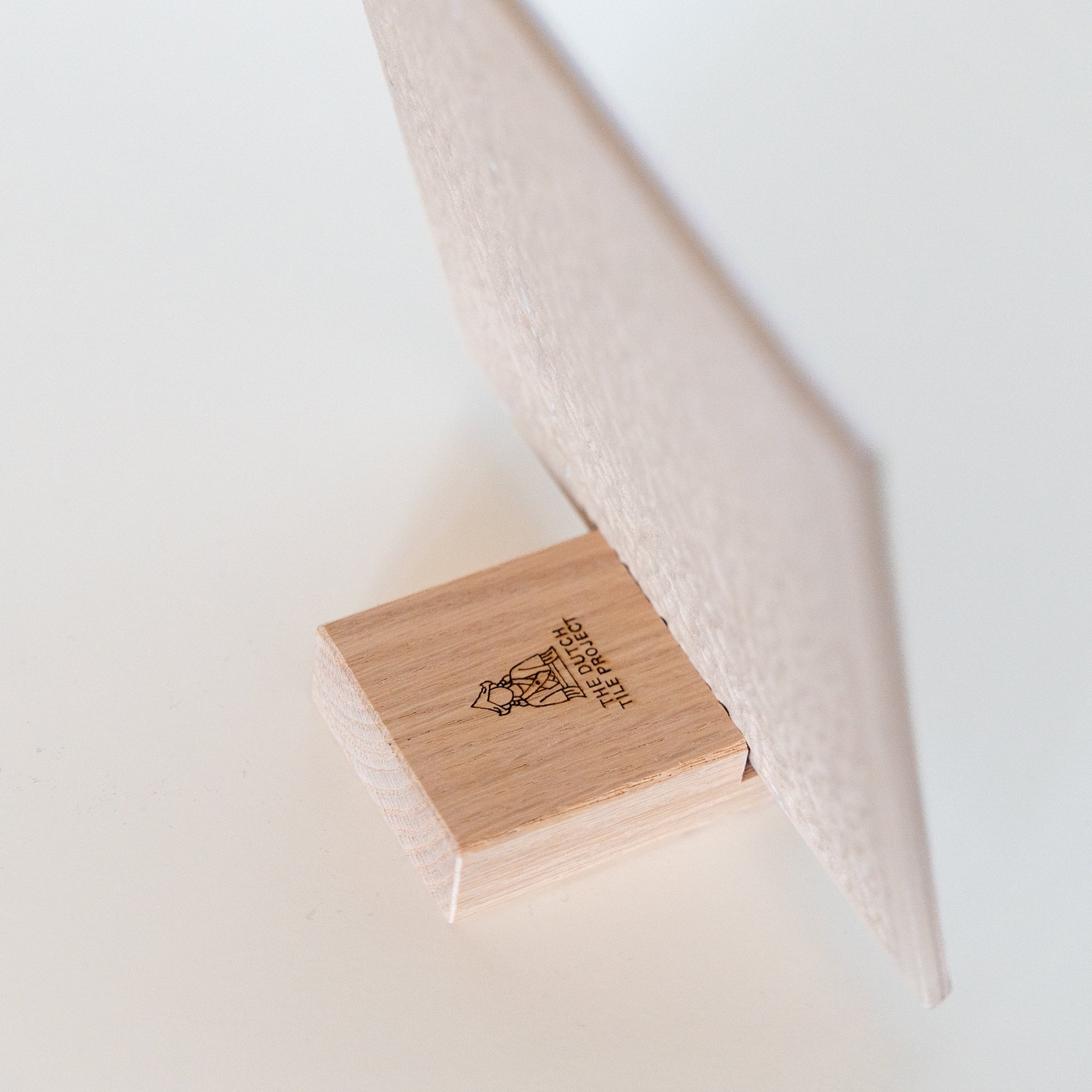 Wooden tile holder with The Dutch Tile Project logo holding a ceramic tile on a light background