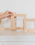 Back view of three wooden tile frames without tiles, with a hand placing the medium-sized frame upright.