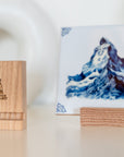Delft Blue hummingbird tile displayed in a wooden tile holder next to a second wooden holder with The Dutch Tile Project logo