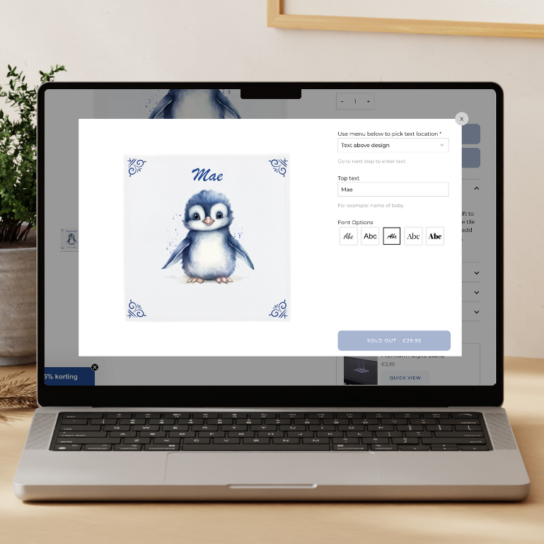 Laptop on a wooden desk displaying a custom tile design window with a penguin illustration and personalised text.